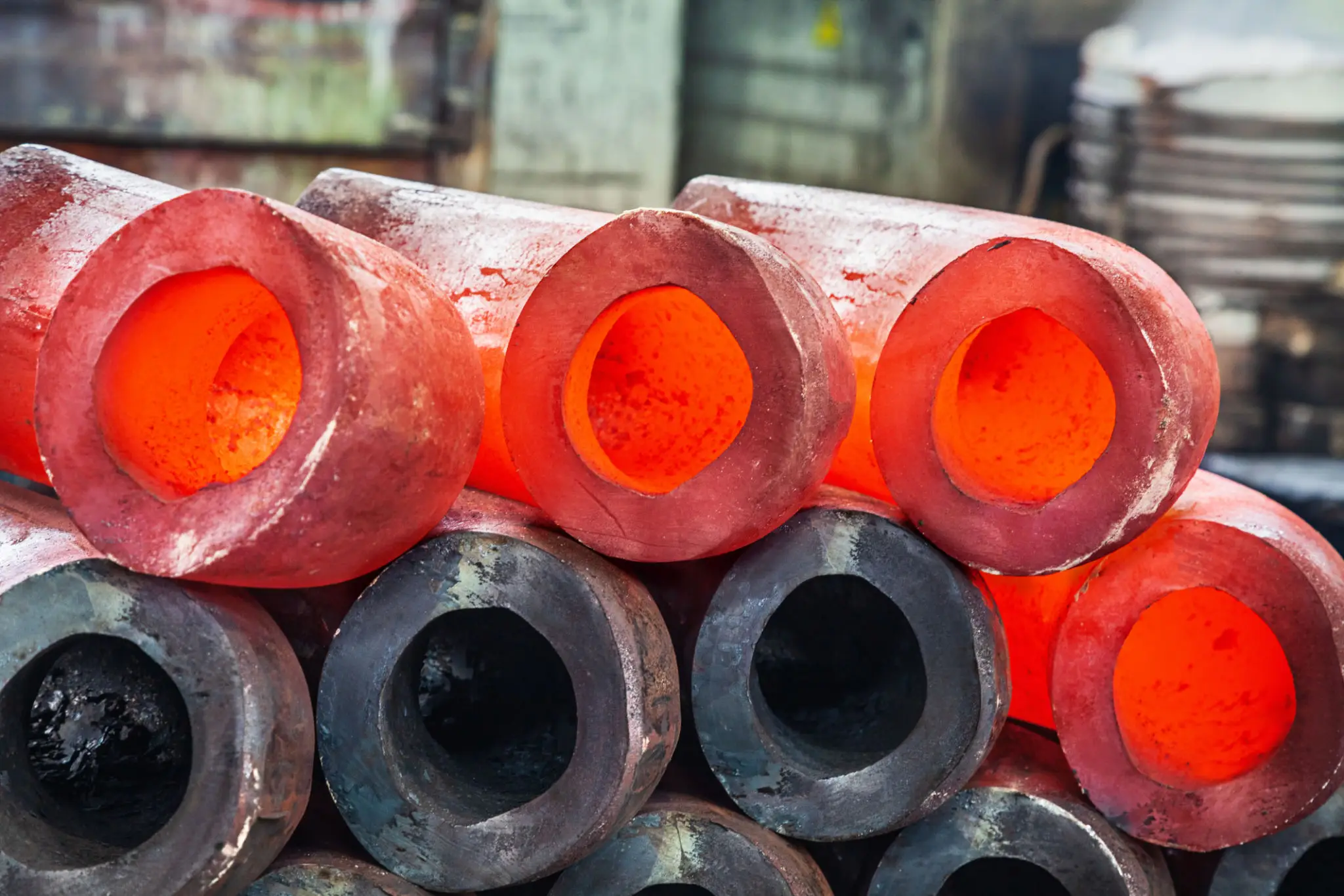 Stack of glowing hot metal rods and cooled rods in a factory.