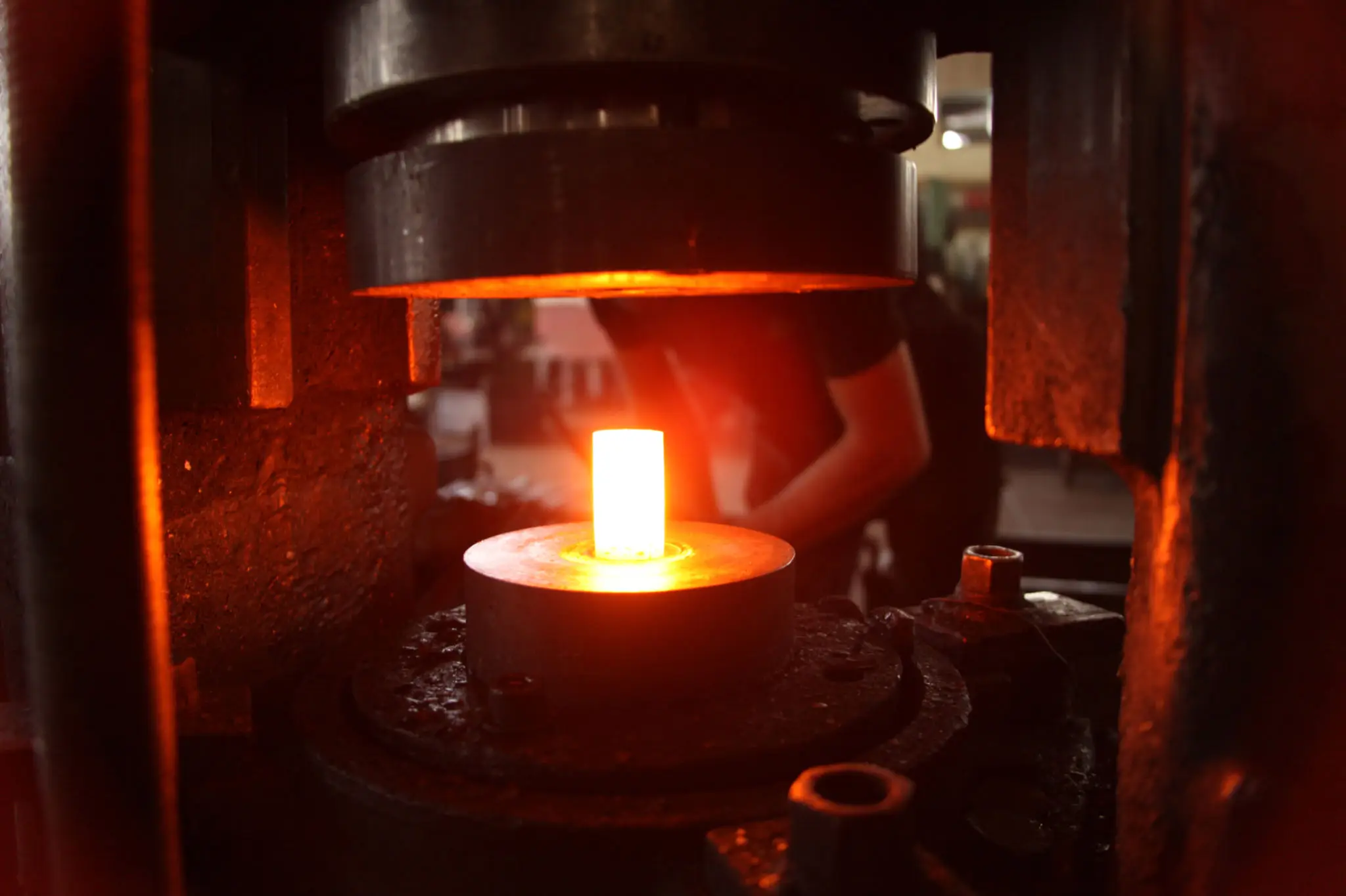 Glowing hot metal being shaped in an industrial forge.